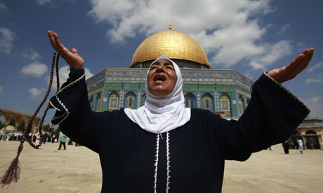 A Palestinian woman prays in front of the Dome of the Rock in Jerusalem's Old City