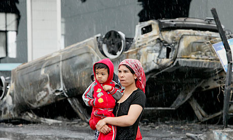A Uighur woman and child walk past a charred car in Urumqi after riots exploded in July 2009