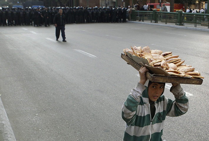 egpyt protests: A boy carrying bread on his head runs away from a column of riot police