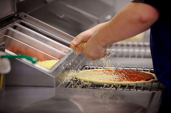 Business week in pictures: Cheese topping being added to a fresh pizza at a take away pizza store