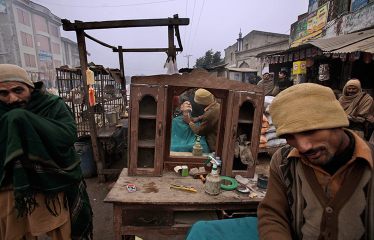 24 hours in pictures: A Pakistani street barber gives a haircut to a customer