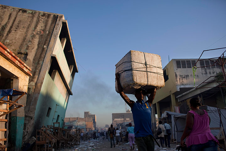 24 hours in pictures: A man carries a box on his head past quake-damaged buildings, Haiti