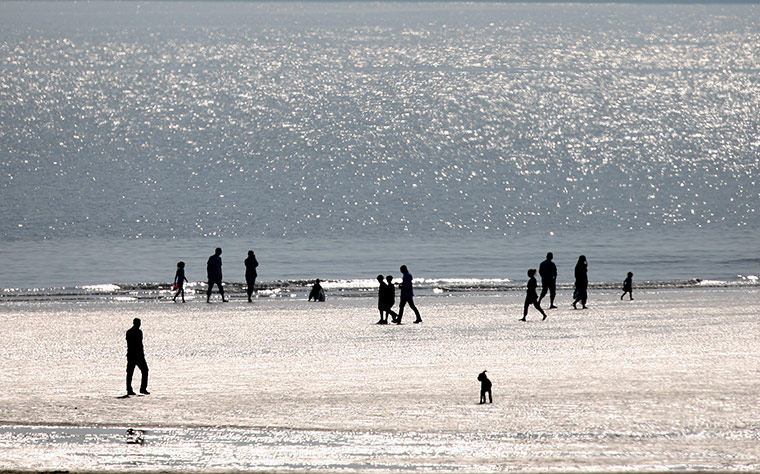 Weather: Member's of the public are seen silhouetted as they walk along the beach