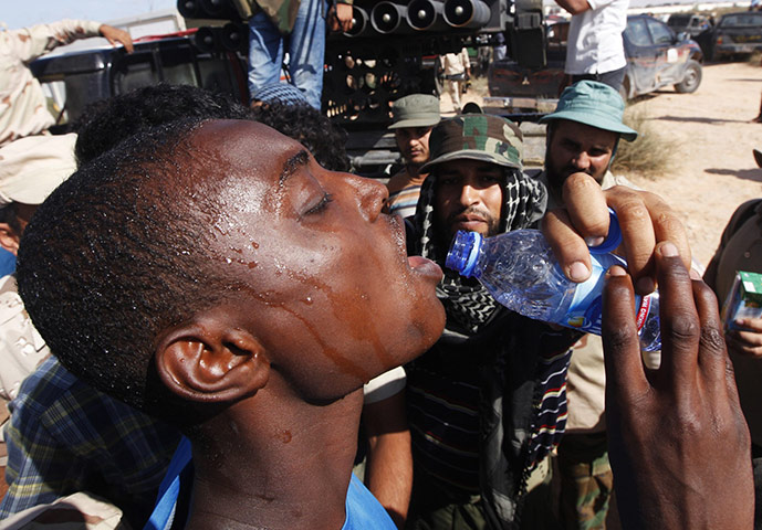 Sirte battles: A pro-Gaddafi fighter drinks water after he was taken prisoner 