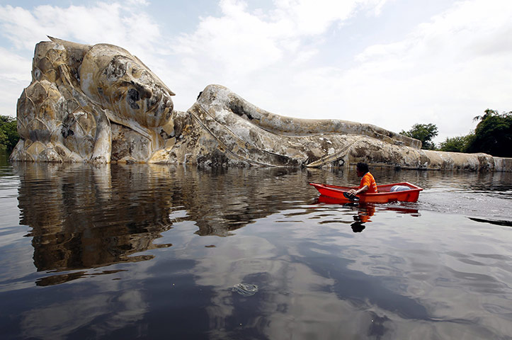 Flooding in Thailand: A resident rows a boat past a submerged Buddha statue