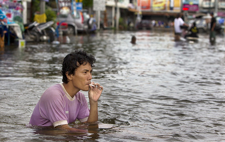 Thailand floods: A man smokes a cigarette as he sits in the flooded streets, Thailand