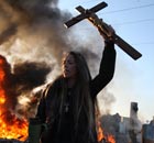 An activist holds up a crucifix as a barricade burns during evictions from Dale Farm travellers camp