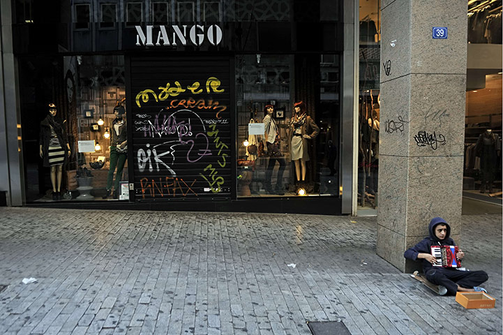 Greece strikes & protests: A boy plays accordion in front of a closed shop in an Athens shopping area