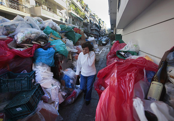 Greece strikes & protests: A woman covers her nose as she walks by a wall of piled-up rubbish