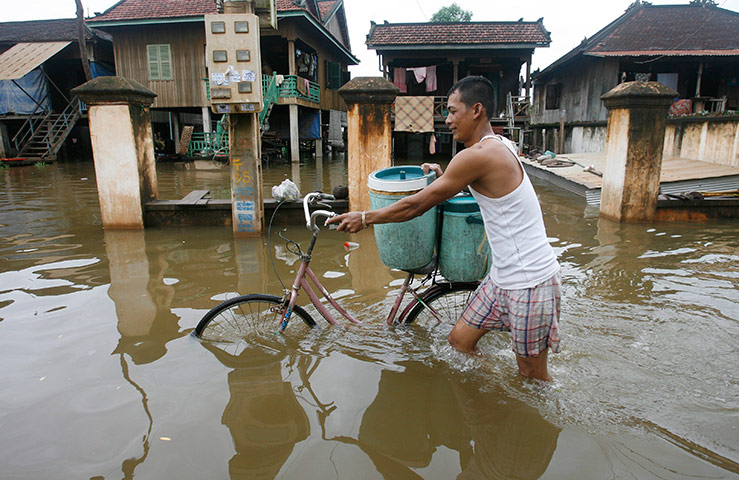 Cambodia floods: A Cambodian man walks with his bicycle though a flooded street