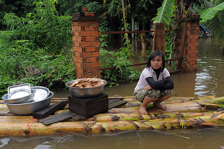 Cambodia floods: A Cambodian girl crouches on a raft with food supplies at Kian Svay