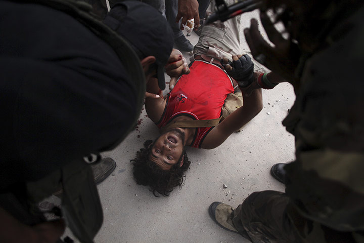 Sirte falls: A wounded Libyan rebel fighter is helped by other fighters