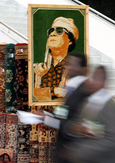 Cult of Gaddafi: Delegates walk in front of a framed carpet showing Gaddafi 