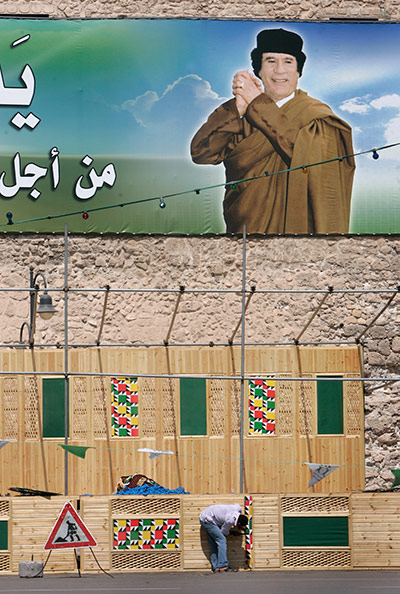 Cult of Gaddafi: A worker builds a wooden podium in front of a large poster of Gaddafi 
