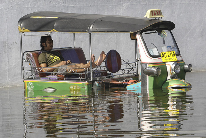 thailand flooding: A tuk tuk driver rests in his partially submerged vehicle in Bangkok 