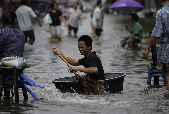 bangkok flooding: A man uses a broom to paddle along a street