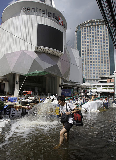Bangkok: A Thai man wades along floods in front of a shopping plaza in Bangkok