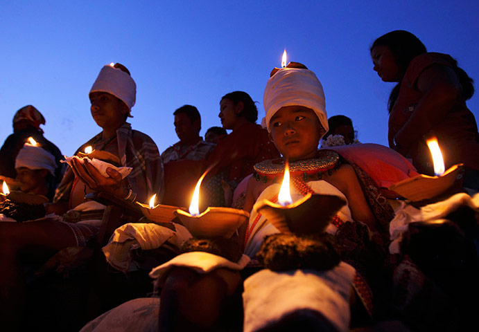 24 hours: Bhaktapur, Nepal: A boy sits with lighted oil lamps while offering prayers