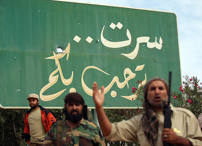 sirte: Rebels stand in front a a sign that reads in Arabic, Sirte Welcomes You 