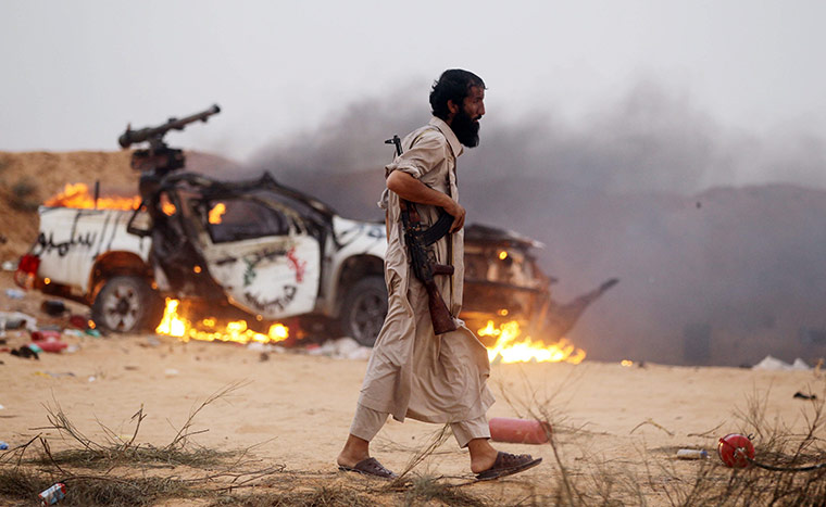 sirte: A rebel walks past a vehicle destroyed by pro-Gadaffi fighters 