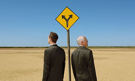 Two businessmen with briefcases standing by road sign in desert