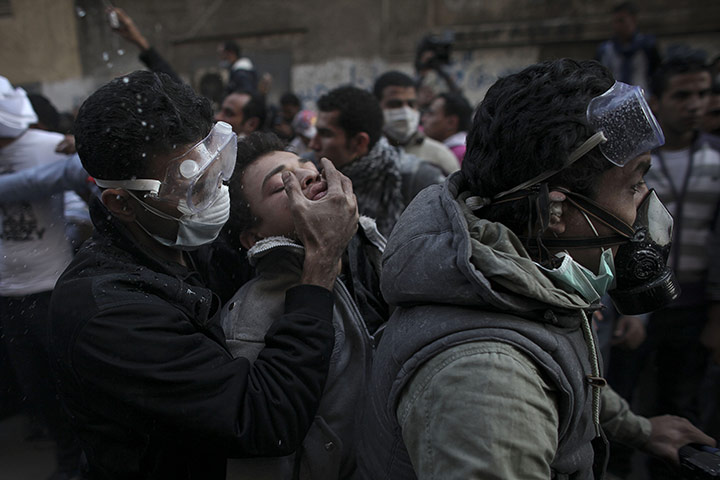 Egypt protests day 4: A protester overwhelmed by tear gas is aided by two men on a motorcycle 