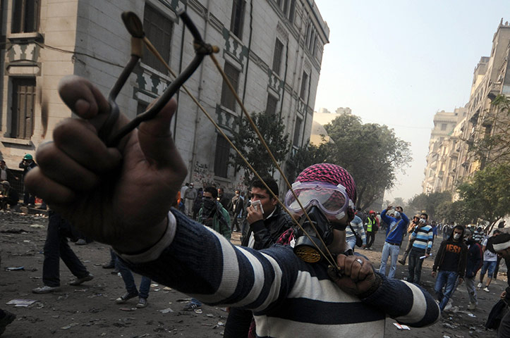 Egypt protests day 4: An Egyptian youth wearing a gas mask aims a sling shot during clashes