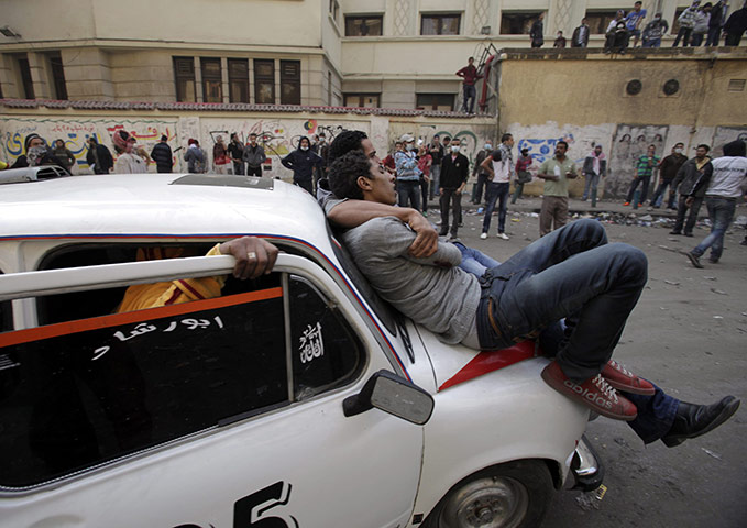 Egypt protests day 5: Two Egyptian protesters affected by teargas lean on a car