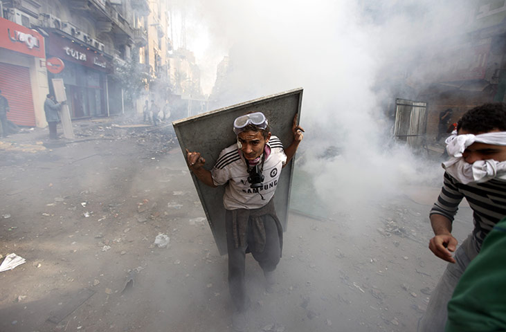Egypt protests day 5: An Egyptian protester using metal as a shield takes cover from tear gas