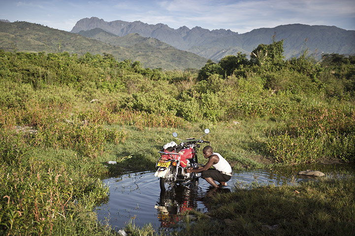 Uganda: A young man washes his motorbike in a stream from the Mountains of the Moon