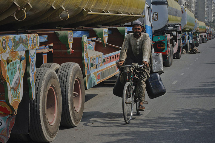 Pakistan NATO raids: A man rides his bicycle past trucks, lined up along a road in Karachi