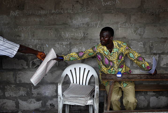 24 hours in pictures: An Election commission official hands a Congolese voter a ballot, Kinshasa