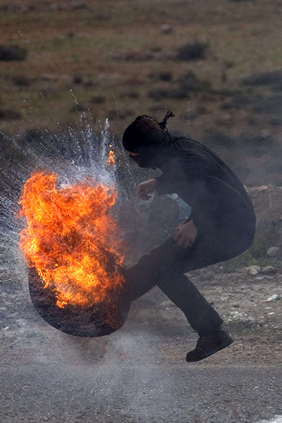 24 hours: A Palestinian demonstrator kicks a burning tyre towards Israeli soldiers