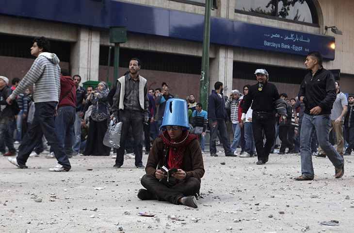 Tahrir Square clashes: A protester shields himself with a bucket while reading the Qur'an