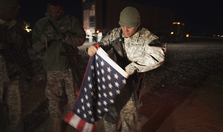 FTA: Lucas Jackson: A soldier folds up a US flag before leaving Camp Adder 