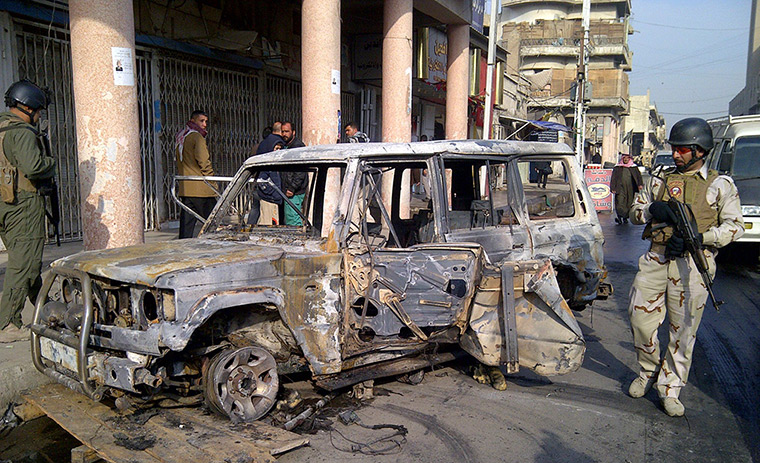Iraq bombing: A soldier stands guard near a burnt vehicle after a bomb, Alawi district