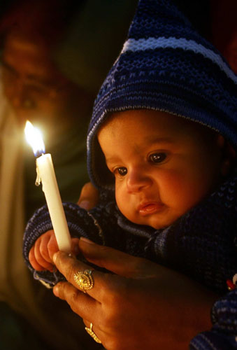 24 hours in pictures: Jammu, India: A child and his mother light a candle during Christmas prayers
