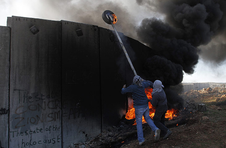 24 Hours: Palestinian demonstrators use a plank to get a burning tyre over the wall