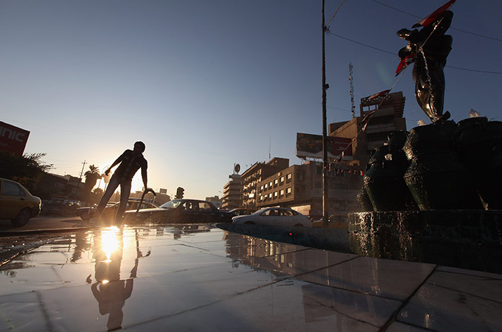 24 hours in pictures: Baghdad, Iraq: A worker uses a hose by a statue in Kahramana Square 