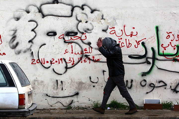 libya unrest: An anti-government demonstrator passes by graffiti in Benghazi