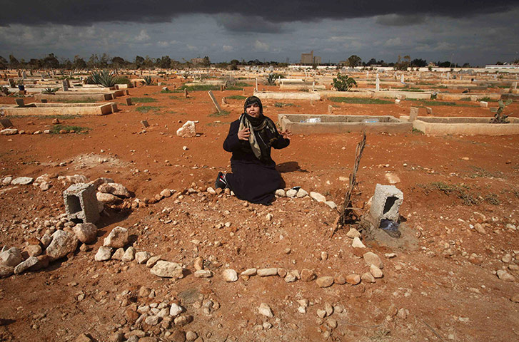 Libya 26 Feb: The mother of a Libyan killed in the recent clashes sits next to his grave