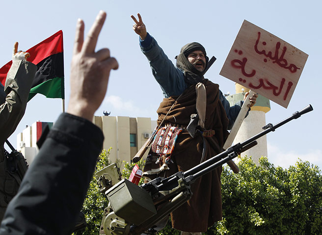 Libya: A man stands on an army tank in the town of Zawiyah. His sign, written in Arabic, reads: 