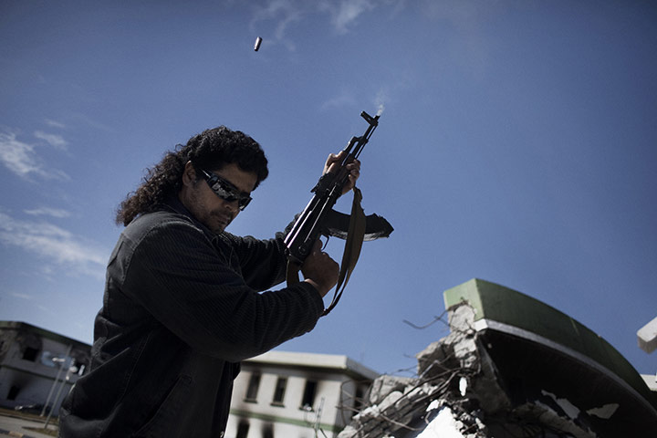 Libya: An armed man shoots in the air at a destroyed army barracks in Benghazi