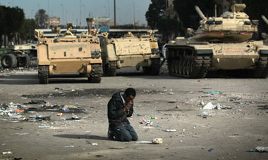 An anti-government demonstrator prays near army vehicles in Cairo, Egypt