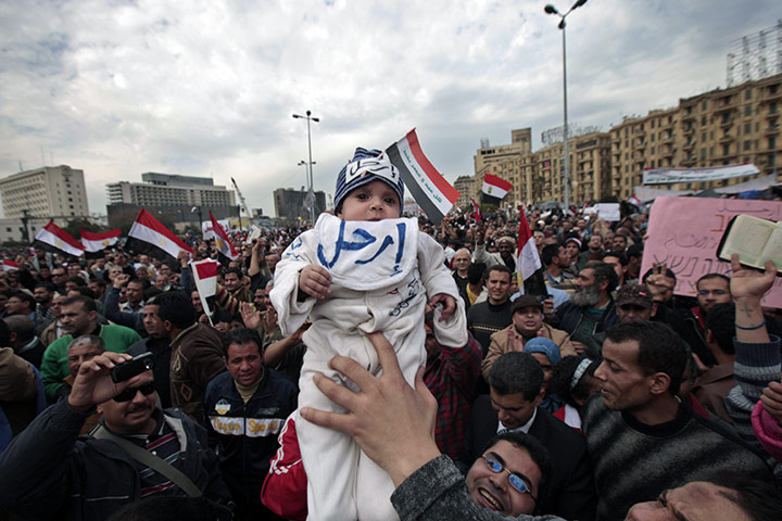 Egypt protests day 13: An anti-government demonstrator holds a baby wearing a hat saying 'Leave'