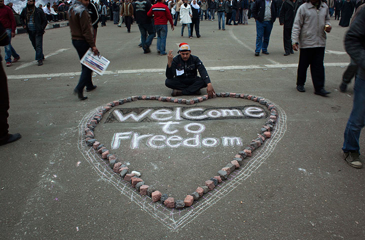 Egypt day 14: An Egyptian anti-Mubarak protesters sits next to graffiti in Tahrir Square