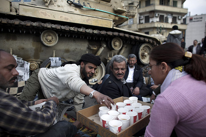 Egypt protests day 15: A volunteer serves tea to protesters as they sit in front of a tank 