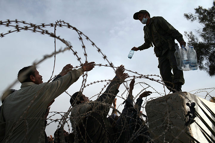 24 hours in pictures: Men wait for water to be thrown to them while waiting to enter Tunisia