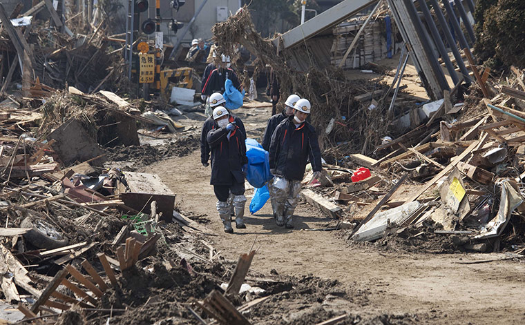 Dan Chung in Japan: Rescue workers carry a body bag through destruction