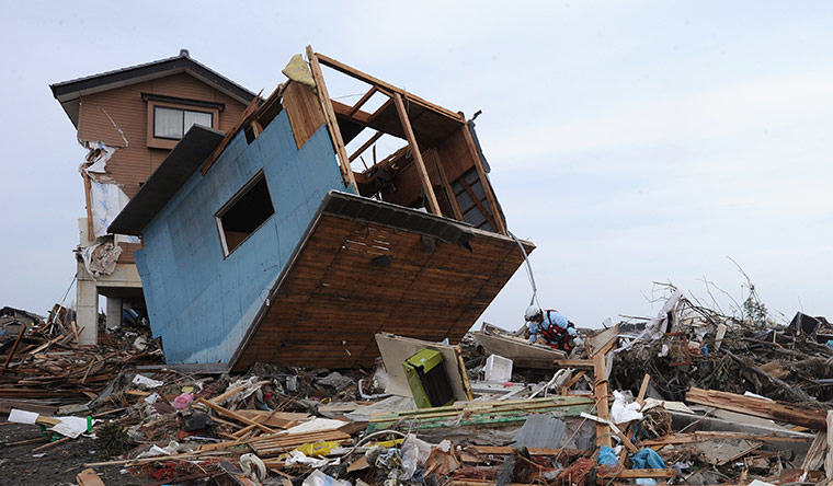 japan disaster aftermath: Rescue workers search for bodies under an upturned house in Natori